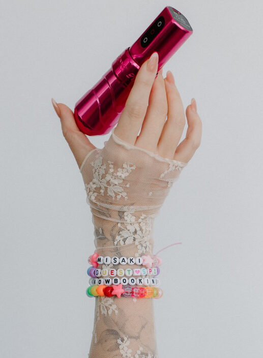 hand with colorful beaded bracelets holding tattoo machine